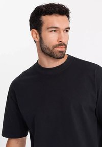 Černé tričko s krátkým rukávem, vyrobené z hladké bavlny, s kulatým výstřihem a volným střihem, vystavené na čistém bílém pozadí.