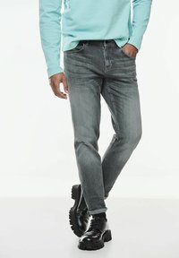 Grå denimjeans med smal passform, subtil blekning, femfickorsdesign, tillsammans med svarta oxfordskor och en ljusblå långärmad skjorta.