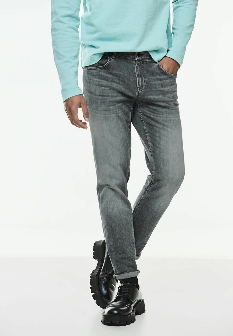 Grå denimjeans med smal passform, subtil blekning, femfickorsdesign, tillsammans med svarta oxfordskor och en ljusblå långärmad skjorta.