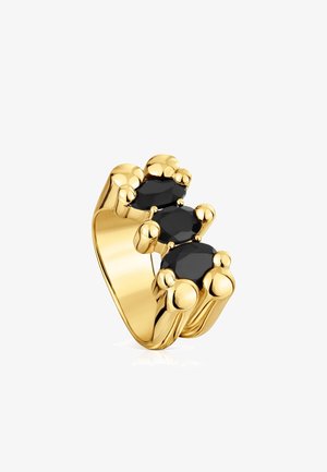 Bague en métal doré mettant en avant trois pierres noires taillées en forme allongée, avec un design texturé et arrondi sur l'anneau.