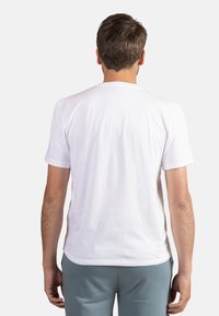 Biała bawełniana koszulka z okrągłym dekoltem i krótkimi rękawami, o gładkiej teksturze. Widoczne szwy wzdłuż dołu i ramion.