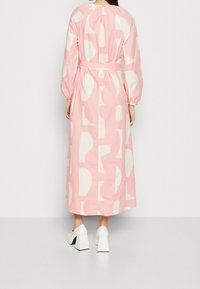 Dlouhé růžové bavlněné šaty s bílými abstraktními tvary, vybavené nabíranými rukávy a páskem v pase. Hladká textura s volnějším střihem.