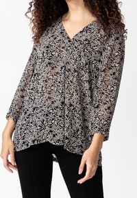 Blusa floreale in bianco e nero con scollo a V, maniche lunghe e silhouette fluida, realizzata in tessuto leggero e trasparente.