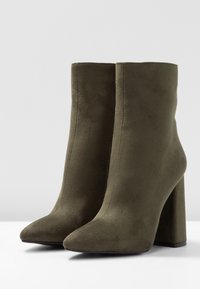Bottines vert olive en suède doux, avec un bout pointu et un talon épais et haut. Texture lisse sans matériel visible.
