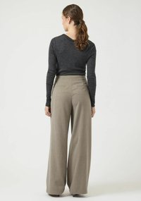 Top grigio a maniche lunghe abbinato a pantaloni beige a gamba larga a vita alta, caratterizzati da una texture sottile e due tasche posteriori.