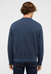 Sweat-shirt bleu marine avec poignets et ourlet côtelés. Design simple, texture douce, détail de l'étiquette à l'arrière, assorti à un jean foncé.