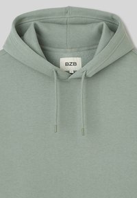 Haut à capuche vert clair en tissu doux, avec une capuche à cordon de serrage, des poignets côtelés et une étiquette avec la marque 'BZB' à l'intérieur.