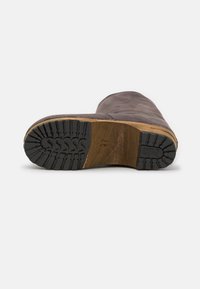 Brun läderkänga med ovandel i mocka, träklack och svart gummisula med ett mönstrat mönster för grepp och stabilitet.