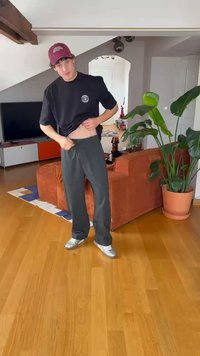 Sort t-shirt, grå brede bukser og sølv sneakers. T-shirten har et rundt logo; bukserne har en justerbar talje.