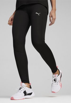 Leggings negros de material elástico, con un discreto logo blanco. Combinados con zapatillas blancas y negras con acentos rosas.