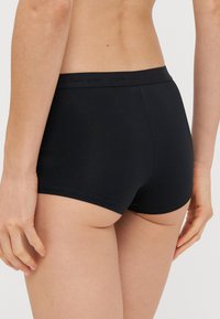 Fekete pamut boxer nadrág sima textúrával és rugalmas derékkal, amelyen a márkaneve található. Minimális dizájn, nincs látható minta.