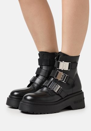 Bottines en cuir noir avec trois boucles décoratives en argent, une semelle épaisse et un logo embossé au niveau du talon.