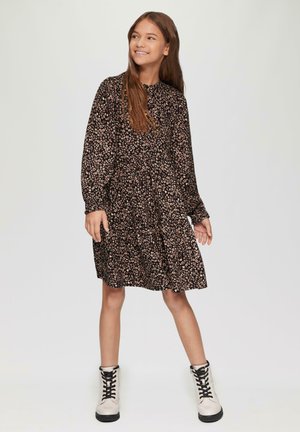 Schwarzes Blumenmusterkleid mit langen Ärmeln, geraffter Taille und gestuftem Rock. Kombiniert mit cremefarbenen Kampfstiefeln mit schwarzen Schnürsenkeln.