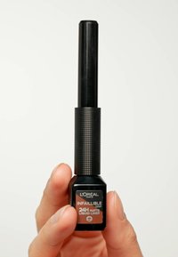 Liner liquido opaco Infallible Grip di L'Oréal in una bottiglia nera con un tappo testurizzato. L'etichetta presenta un font bronzo con dettagli su come utilizzare il prodotto.