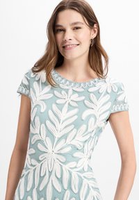 Hellblaues Kleid mit weißer Blumenstickerei, kurzen Ärmeln und einem gewellten Halsausschnitt. Der Stoff hat eine glatte Textur.