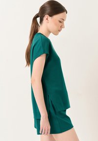 Groene katoenen blend top met korte mouwen, zijsplitten en een relaxte pasvorm, gecombineerd met bijpassende shorts. Gladde textuur en minimalistisch ontwerp.