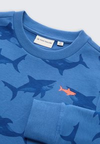 Felpa blu con motivi di squali in blu scuro, con un piccolo accento di pesce arancione. Polsini e scollo a costine testurizzati. Etichetta del marchio visibile.