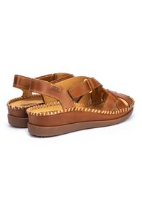 Sandalias de cuero marrón con un diseño de tiras, costuras texturizadas y una suela acolchada. Cuenta con correas ajustables y punta abierta.