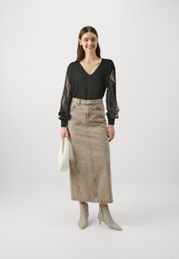 Svart bluse med blondermer, V-hals; beige denim maxiskjørt; lysegrå ankelstøvler; hvit veske. Glatte teksturer og tettsittende design.