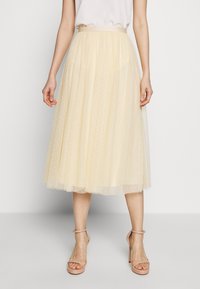 Jupe midi en tulle jaune avec taille froncée, motif à pois, design superposé et texture transparente, associée à des talons nus à brides.