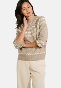 Beiger Pullover mit weißen geometrischen Mustern, rundem Ausschnitt und lässigem Schnitt. Stricktextur mit umgeschlagenen Ärmeln und geripptem Saum.