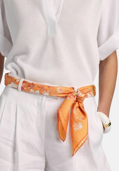 Écharpe en soie à motif floral orange nouée en ceinture, mettant en valeur un haut en maille blanche et un pantalon de couleur claire, avec une texture lisse.