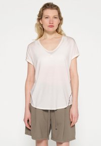 Lyserød, kortærmet V-hals t-shirt i blødt stof, med en enkelt knapdetalje og en buet kant. Sammen med olivenfarvede shorts.