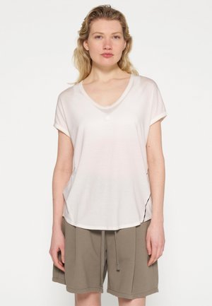 Lichtroze, kort boord V-hals t-shirt van zachte stof, voorzien van een enkele knoopdetail en een gebogen zoom. Gecombineerd met olijfgroene shorts.
