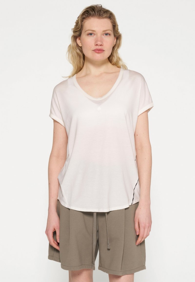 Lyserød, kortærmet V-hals t-shirt i blødt stof, med en enkelt knapdetalje og en buet kant. Sammen med olivenfarvede shorts.