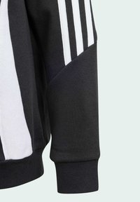 Sweatshirt noir avec un design à rayures blanches, présentant un poignet côtelé et une texture douce. Découpe diagonale distincte à l'épaule.