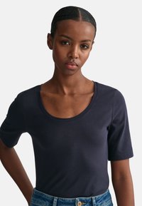 Marineblå kortærmet T-shirt lavet af glat, strækbart stof med en rund halsudskæring og tætsiddende silhuet, kombineret med denim jeans.