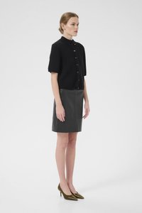 Must have lühikeste varrukatega nööpidega kudumtop ja liibuv must nahkne mini-seelik. Modelli jalas on oliivrohelised terava ninaga kõrged kontsad.