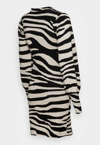 Neulemekko, jossa on rohkea musta-valkoiseksi raidoitettu seeprahihappo, pitkät hihat, korkea kaula-aukko ja hieman levenevä helma.