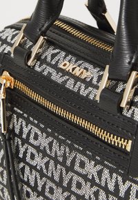 Black and white handbag featuring DKNY branding, textured fabric, gold accents, and a zippered pocket with a golden zipper.