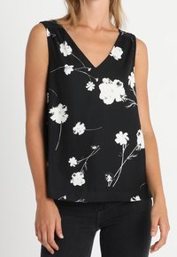 Top senza maniche nero con scollo a V decorato da motivi floreali bianchi. Realizzato in tessuto morbido con una vestibilità rilassata.