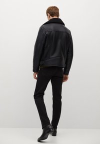 Giubbotto di pelle nera con colletto in shearling, design aderente e dettagli di cucitura sottili. Abbinato a pantaloni neri e stivali alla caviglia.