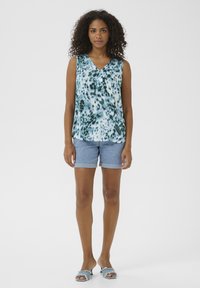 Débardeur sans manches avec un imprimé animal bleu et vert, en col en V, associé à un short en denim retroussé et des sandales glissantes bleu clair.
