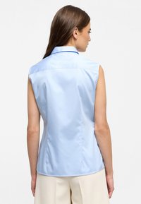 Camicia senza maniche di colore blu chiaro, con colletto, texture liscia e pince posteriori per una vestibilità sartoriale.