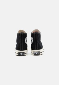 Svarte kanvas høye sneakers har hvite sømmer, rund logolapp på yttersiden og en gummisåle med stjerneakenter.