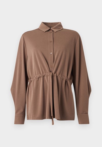 Καφέ πουκάμισο με μακριά μανίκια, εμπρόσθιο κουμπί, κορδόνι στη μέση, κλασικό γιακά και φαρδιά μανσέτα σε λευκό φόντο.