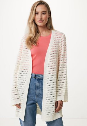 Losse gebreide cardigan van gestructureerd wit garen, met een losse fit, lange mouwen en een open voorkant. G gedragen over een koraalkleurige top en jeans.