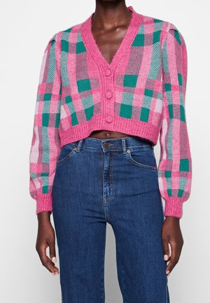 Gros plan sur la taille d'une personne portant un cardigan écossais court rose, vert et blanc avec de gros boutons, et un jean bleu taille haute.
