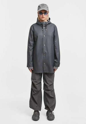 Dark gray waterproof jacket with a hood, snap buttons, and pockets, paired with loose-fitting gray pants and black shoes.
