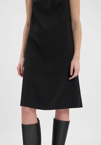 Robe noire sans manches au design simple, texture douce, longueur genou, assortie à des bottes en cuir noires mi-hautes.