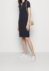 Námořnicky modré polo šaty s krátkými rukávy, s kontrastním límečkem a třemi knoflíky. V kombinaci s bílými teniskami a malou béžovou kabelkou.