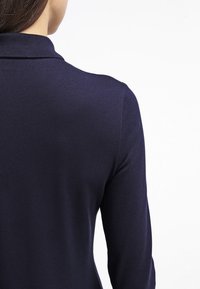 Polo shirt bleu marine en tissu texturé, avec un col et des manches longues, montrant l'arrière avec un design ajusté.