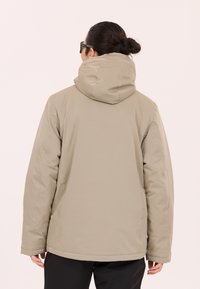 Beige huvjacka med en mjuk textur, med en avslappnad passform och sömmar på axlarna. Bakifrån visar den ingen ytterligare detaljering.