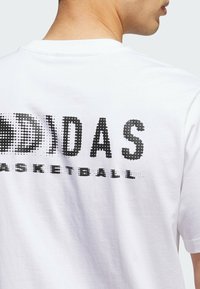 Hvid bomulds T-shirt med et stort sort pixeliseret "ADIDAS BASKETBALL" grafik på ryggen, rund halsudskæring og korte ærmer.
