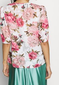 Průhledná bílá blůza s růžovým květinovým vzorem, krátkými nafouklými rukávy a vlnitými lemy, spojená se zelenou saténovou sukní.