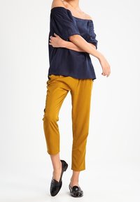 Navy off-the-shoulder top with short sleeves, paired with mustard cropped pants and glossy black loafers. Smooth, lightweight fabric.